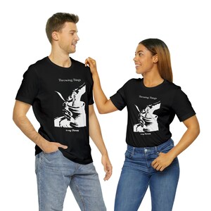 Puede incluir: Dos personas con camisetas negras con un diseño gráfico blanco. El gráfico muestra a una persona lanzando una maceta en un torno de alfarería. El texto de la camiseta dice "Throwing Things is my Therapy".