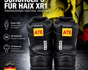 May include: A pair of black leather boots featuring bright yellow rectangular clips attached to the back pull tabs, each displaying the text ATE in bold red letters. The boots include white Gore-Tex labels and a Made in Germany circular emblem.