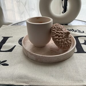Peut inclure: Un bougeoir en céramique rose en forme de gland avec un couvercle. Le bougeoir est posé sur un sous-verre en marbre rose.