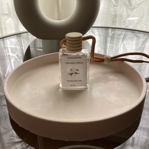 Peut inclure: Une bouteille en verre transparente avec un bouchon en bois et un cordon marron. La bouteille contient un diffuseur de voiture avec le texte "Lhiloocandle Diffuseur voiture Vanille des Iles 10 ml".