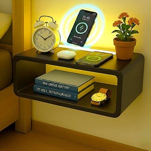 May include: A black floating bedside table with a wireless charging station, alarm clock, and potted plant. Two smartphones are charging wirelessly. The table also holds two books and a wristwatch with a brown leather strap.