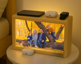 May include: A wooden picture frame with a warm light illuminating a family photo. The photo shows a family of four in a park setting. The frame has a built-in charging station with a phone, wireless earbuds, and a watch.
