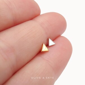 May include: Two small stud earrings in the shape of triangles. One earring is finished in a polished gold tone, while the other is finished in a polished silver tone. The text OLIVE & SKYE is printed in white at the bottom of the image.