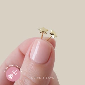 May include: A pair of small gold star-shaped stud earrings with thin posts. The earrings feature a polished metallic finish and a classic five-pointed star design. The text "Stud/Post Earring" and "OLIVE & SKYE" is visible on the image.