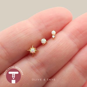 May include: Three gold stud earrings featuring iridescent opal stones. One earring has a four-pointed star setting, one is a round prong-set opal, and one is a small opal paired with a tiny clear stone. The text reads Internally threaded OLIVE & SKYE.