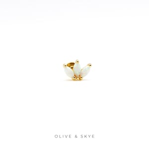 May include: A gold stud earring featuring three marquise-cut white opals arranged in a fan shape, accented with small gold spheres at the base. The text OLIVE & SKYE is printed in black below the jewelry piece on a plain white background.
