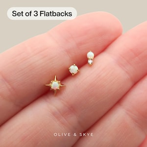 May include: A set of three gold flatback earrings featuring iridescent opal stones. One earring has a four-pointed star setting, one is a simple round opal stud, and the third features a small opal paired with a tiny clear stone. Text reads Set of 3 Flatbacks.