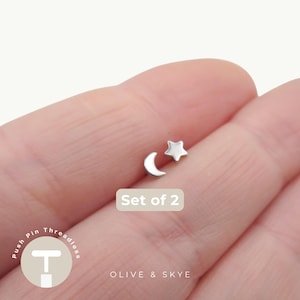 May include: A set of two silver-toned threadless push pin body jewellery pieces, one shaped like a crescent moon and the other like a five-pointed star. The text Set of 2 is visible, along with the brand name Olive & Skye and a logo.