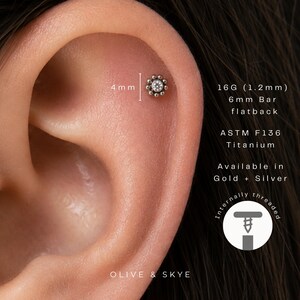 May include: A flower-shaped stud earring with a central clear stone and beaded edges, measuring 4mm in diameter. The jewellery is ASTM F136 titanium, 16G (1.2mm) with a 6mm flatback bar. It is internally threaded and available in gold or silver.