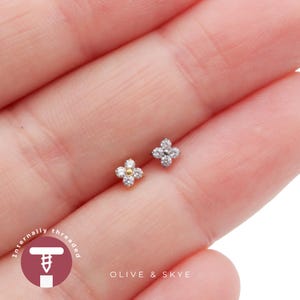May include: Two flower-shaped stud earrings featuring clear, sparkling stones. One earring has a gold centre, while the other has a silver-toned centre. The text "Internally threaded" and "OLIVE & SKYE" is visible in the lower portion of the image.