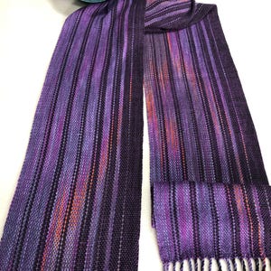 May include: Purple and orange striped woven scarf with black accents and fringe.