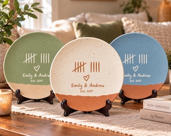 May include: Three round ceramic plates displayed on black stands. Each plate features a speckled finish, a tally mark design, a heart icon, and the text Emily & Andrew Est. 2017. The plates are colored in sage green, cream, and light blue.