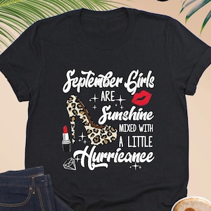 May include: Black t-shirt with a graphic design featuring a leopard print high heel shoe, lipstick, a diamond, and the text "September Girls are Sunshine mixed with a little Hurricance".