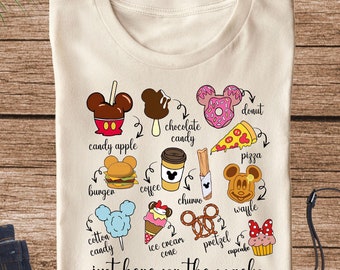 May include: A beige t-shirt with a graphic of Mickey Mouse ears and various Disney snacks, including a candy apple, chocolate candy, burger, coffee, churros, donut, pizza, waffle, cotton candy, ice cream cone, pretzel, and cupcake. The text "just here for the snacks" is printed below the graphic.