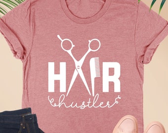 May include: Heather mauve t-shirt with a white graphic of scissors and a comb with the text "HAIR hustlers".