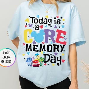 May include: A light blue t-shirt with the text "Today is a CORE MEMORY Day" in colorful letters. The shirt features a Mickey Mouse head and characters from the movie Inside Out.