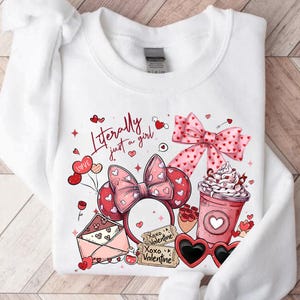 May include: White sweatshirt featuring a Valentine's Day design. The graphic includes a pink bow, heart-shaped sunglasses, a coffee cup, and the text "Literally just a girl." The sweatshirt has a crew neck and long sleeves.
