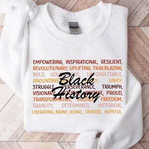 May include: White sweatshirt with the words "Black History" in a stylized font. Surrounding the text are words like "Empowering," "Inspirational," and "Resilient" in a gradient of orange and red.