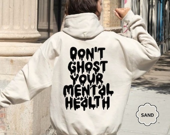 Op de afbeelding: Een witte hoodie met de tekst "DON'T GHOST YOUR MENTAL HEALTH" in zwarte druppelende letters. De hoodie wordt gedragen door een persoon.