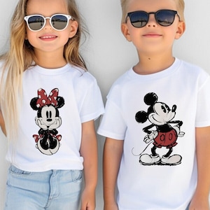 May include: Two children wearing white t-shirts with Disney character graphics. One shirt features Minnie Mouse with a red polka dot bow, and the other features Mickey Mouse in a red outfit. Both are wearing sunglasses.