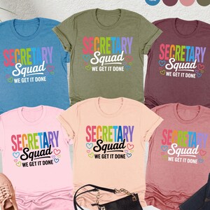 May include: A collection of colorful t-shirts with the text "SECRETARY Squad WE GET IT DONE" in rainbow colors. The shirts are in various colors, including blue, green, pink, peach, and maroon. A pair of sneakers, a purse, and jeans are also in the image.
