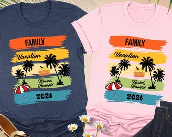 Peut inclure: Deux t-shirts, un bleu marine et un rose, avec un graphisme coloré. Le motif comprend les mots "FAMILY Vacation Kawai Hawaii 2026" avec des palmiers et un parasol. Un jean et des chaussures sont également dans l'image.