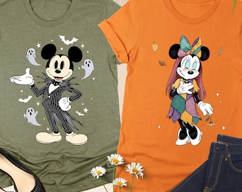 May include: A heather olive t-shirt featuring Mickey Mouse in a pinstripe suit with ghosts and bats, and an orange t-shirt featuring Minnie Mouse in a patchwork dress with autumn leaves. Both shirts are short-sleeved with crew necklines.