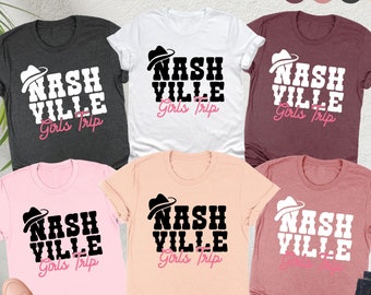 Könnte beinhalten: Fünf T-Shirts in verschiedenen Farben mit dem Text "NASHVILLE Girls Trip" und einer Grafik eines schwarz-weißen Cowboyhuts. Die Shirts sind in den Farben Heather Maroon, Heather Mauve, Dark Grey Heather, Peach und Weiß erhältlich.