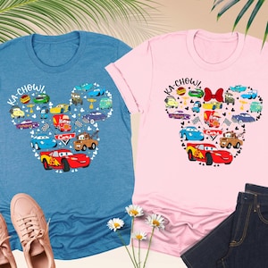 May include: Two t-shirts featuring a Mickey Mouse head design made up of Cars characters. The left shirt is blue and the right shirt is pink. The shirts say "Ka-Chow!" and have a Cars logo.