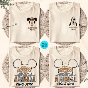 May include: Two beige t-shirts with a safari theme. The front of the shirts feature Mickey Mouse and Goofy wearing safari hats. The back of the shirts feature a Mickey Mouse head with the text "Animal Kingdom" inside the ears. The Mickey Mouse head is surrounded by animal print.