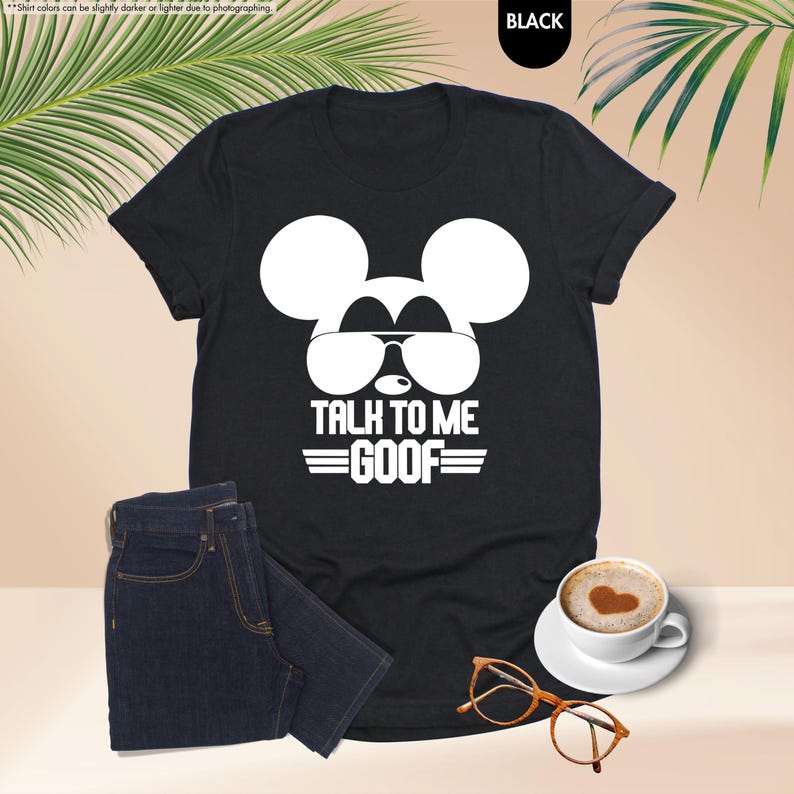 May include: Black t-shirt featuring a white Mickey Mouse graphic wearing sunglasses and the text "TALK TO ME GOOF". The image includes dark wash jeans, a coffee cup, and a pair of spectacles.