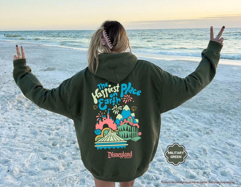 Pu&ograve; includere: Una felpa con cappuccio verde con una stampa grafica del castello di Disneyland e il testo "The Happiest Place on Earth".