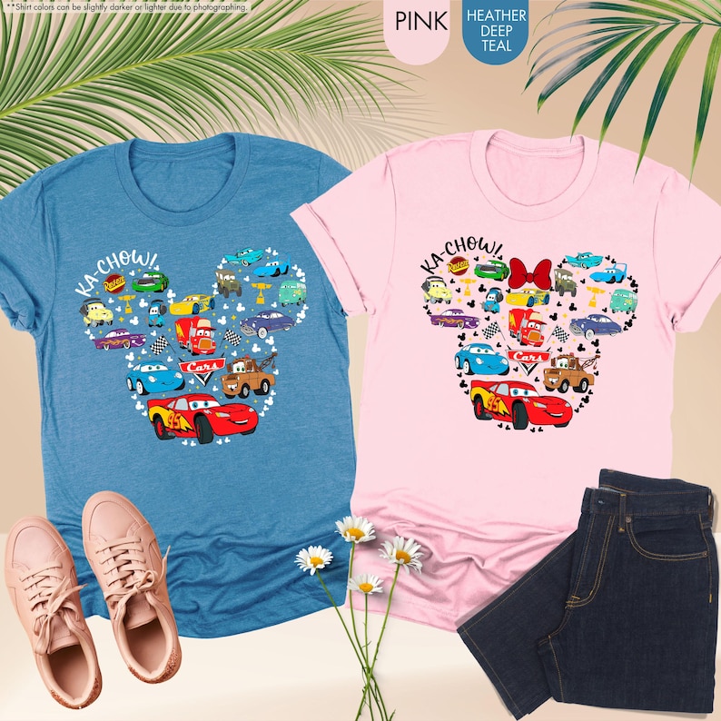 May include: Two t-shirts featuring a Mickey Mouse head design made up of Cars characters. The left shirt is blue and the right shirt is pink. The shirts say "Ka-Chow!" and have a Cars logo.