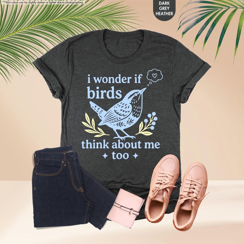 May include: A dark grey heather t-shirt featuring a light blue graphic of a bird and the text 'i wonder if birds think about me too' with a small heart in a thought bubble, paired with dark blue denim shorts and light pink sneakers.