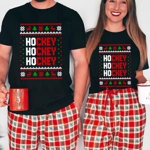 May include: A couple wearing matching black t-shirts with a red and white Christmas-themed design that says "HOCKEY" three times. They are also wearing red and white plaid pajama pants.