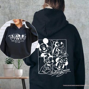 May include: Black hoodie featuring a white graphic of Mickey Mouse and friends. The front of the hoodie displays "MICKEY & CO Est. 1928". The back has a four-panel design with Mickey, Goofy, Donald, and Minnie Mouse. A classic Disney-themed apparel item.