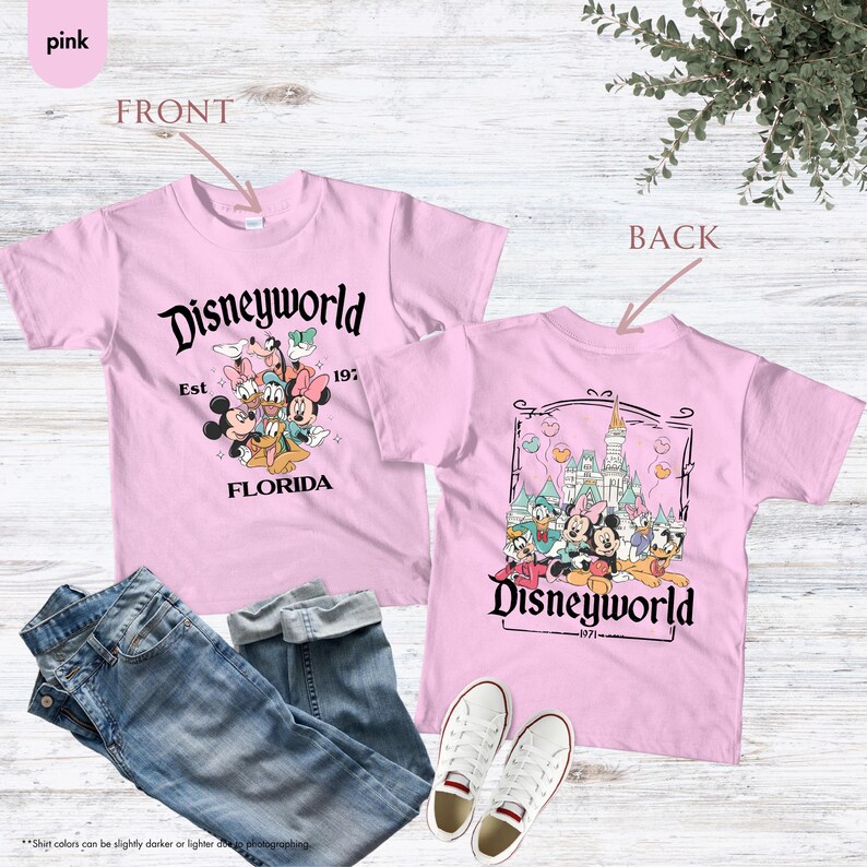 May include: Pink t-shirt with a Disneyworld graphic on the front and back. The front graphic features Mickey, Minnie, Donald, Daisy, and Goofy. The back graphic shows the Disneyworld castle and characters. Includes the text "Disneyworld Florida 1971".