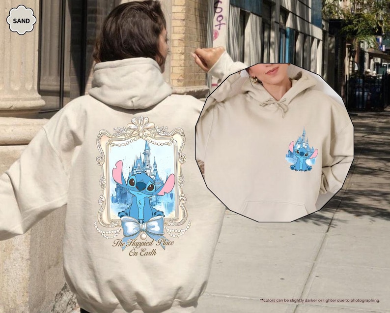 May include: Sand-colored hoodie featuring a blue cartoon character and castle design. The back of the hoodie displays a framed image of the character and castle with the text "The Happiest Place On Earth". A smaller version of the design is on the front.