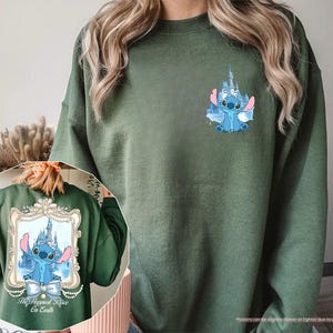 May include: Military green sweatshirt featuring a blue cartoon character with a castle graphic. The design is repeated on the back within a decorative frame, with the text "The Happiest Place on Earth". The sweatshirt is a solid color with a crew neck.