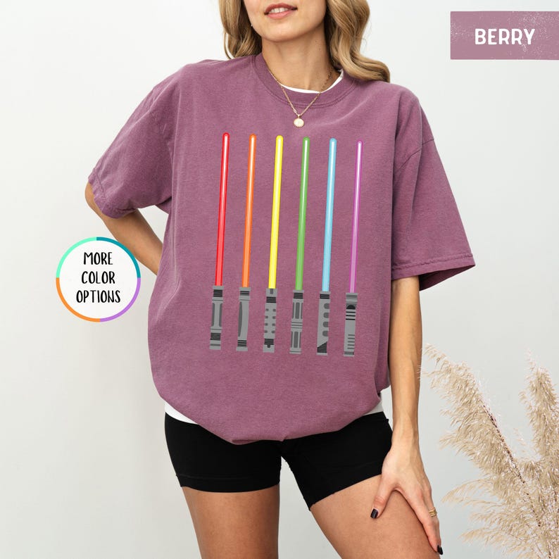 K&ouml;nnte beinhalten: Beerenfarbenes T-Shirt mit einer Grafik von sechs farbenfrohen Lichtschwertern in Regenbogenanordnung. Die Lichtschwerter sind rot, orange, gelb, gr&uuml;n, blau und lila. Das Shirt hat einen Rundhalsausschnitt und kurze &Auml;rmel.