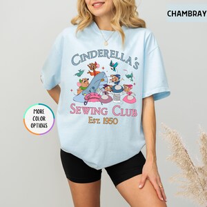May include: Light blue t-shirt with a graphic of mice from Cinderella sewing. The text reads "Cinderella's Sewing Club Est. 1950".