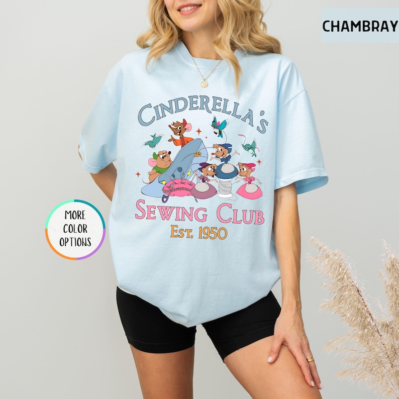 May include: Light blue t-shirt with a graphic of mice from Cinderella sewing. The text reads "Cinderella's Sewing Club Est. 1950".