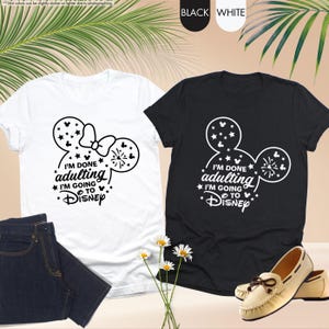 May include: Two t-shirts with a black and white Mickey Mouse design. The white t-shirt has a bow on the Mickey Mouse ears. The black t-shirt has a firework design. Both shirts have the text "I'm done adulting I'm going to Disney".