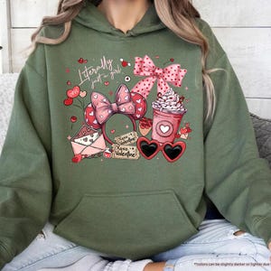 May include: Military green hoodie with a graphic featuring a pink bow, heart-shaped sunglasses, a coffee cup, and the text "Literally just a girl." The design includes hearts and the words "Xoxo Valentine."