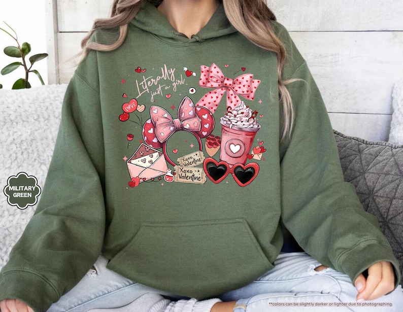 May include: Military green hoodie with a graphic featuring a pink bow, heart-shaped sunglasses, a coffee cup, and the text "Literally just a girl." The design includes hearts and the words "Xoxo Valentine."