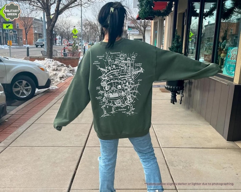 May include: A green sweatshirt with a white graphic print of a flying machine with intricate details. The graphic is a detailed line drawing of a flying machine with a large central structure and multiple smaller structures attached to it. The sweatshirt is a casual style with a crew neck and long sleeves.
