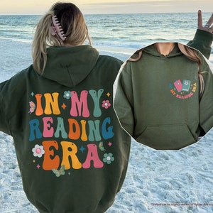 a woman standing on a beach wearing a green hoodie