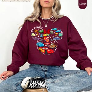 May include: A maroon sweatshirt featuring a graphic of Mickey Mouse's head made up of characters from the Disney film Cars. The text "KA-CHOW!" and "Cars" are included in the graphic.