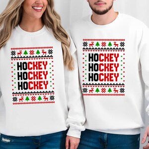 May include: White Christmas sweater with a red and black "HOCKEY" design. The sweater has a festive pattern with green trees and reindeer.