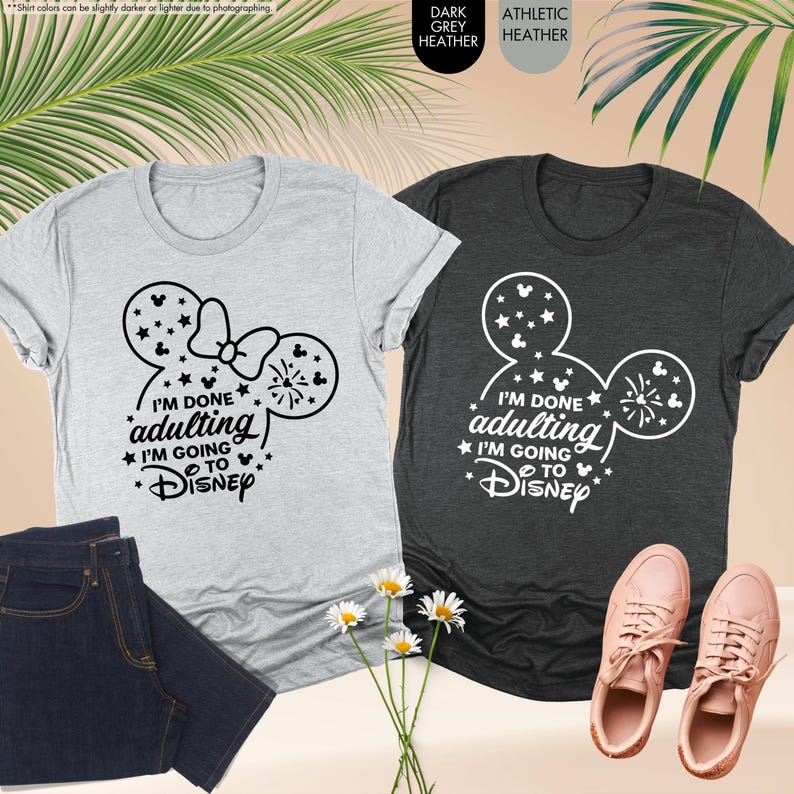 May include: Two t-shirts with a Mickey Mouse ear design and the text "I'm done adulting I'm going to Disney". The shirt on the left is light grey heather and the shirt on the right is dark grey heather.